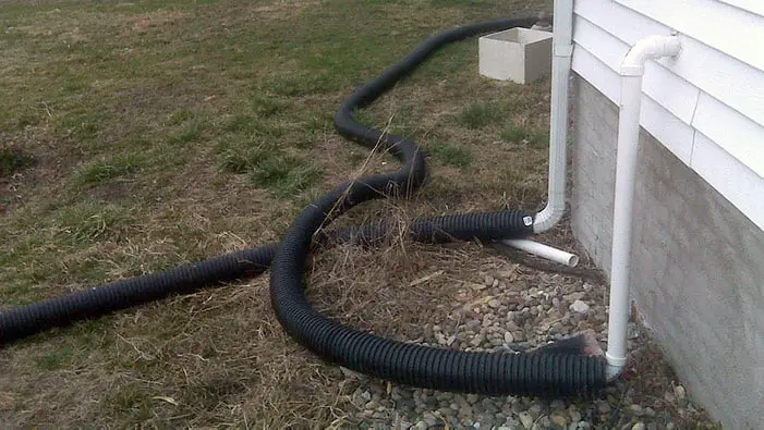 Discharge pipe connected to the sump pump system in a yard next to the foundation of a building