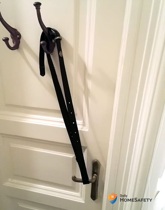 A bathroom door with a belt stretched between the handle and the hook mounted on the door 