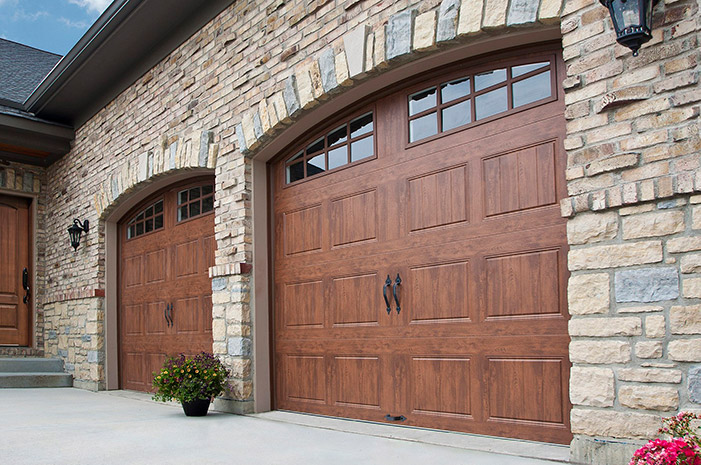 Swing-out wood garage doors with windows and vertical lines in front of a brick building