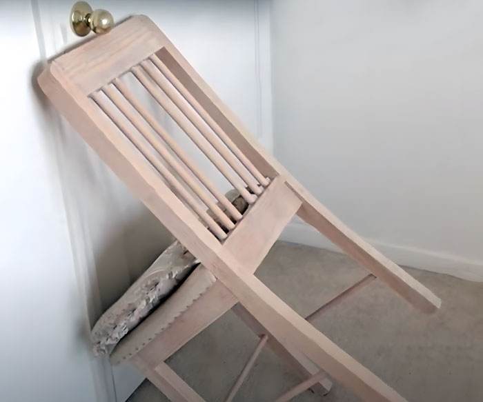 Wooden chair turned around, tilted, and wedged under the doorknob