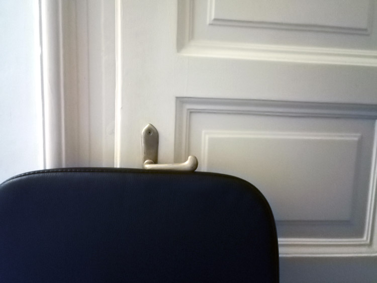 The back of a black office chair placed tightly under the lever of a door