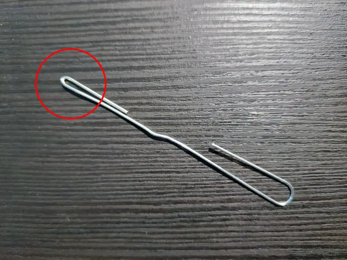 A modified paperclip on a black table with one end circled in red